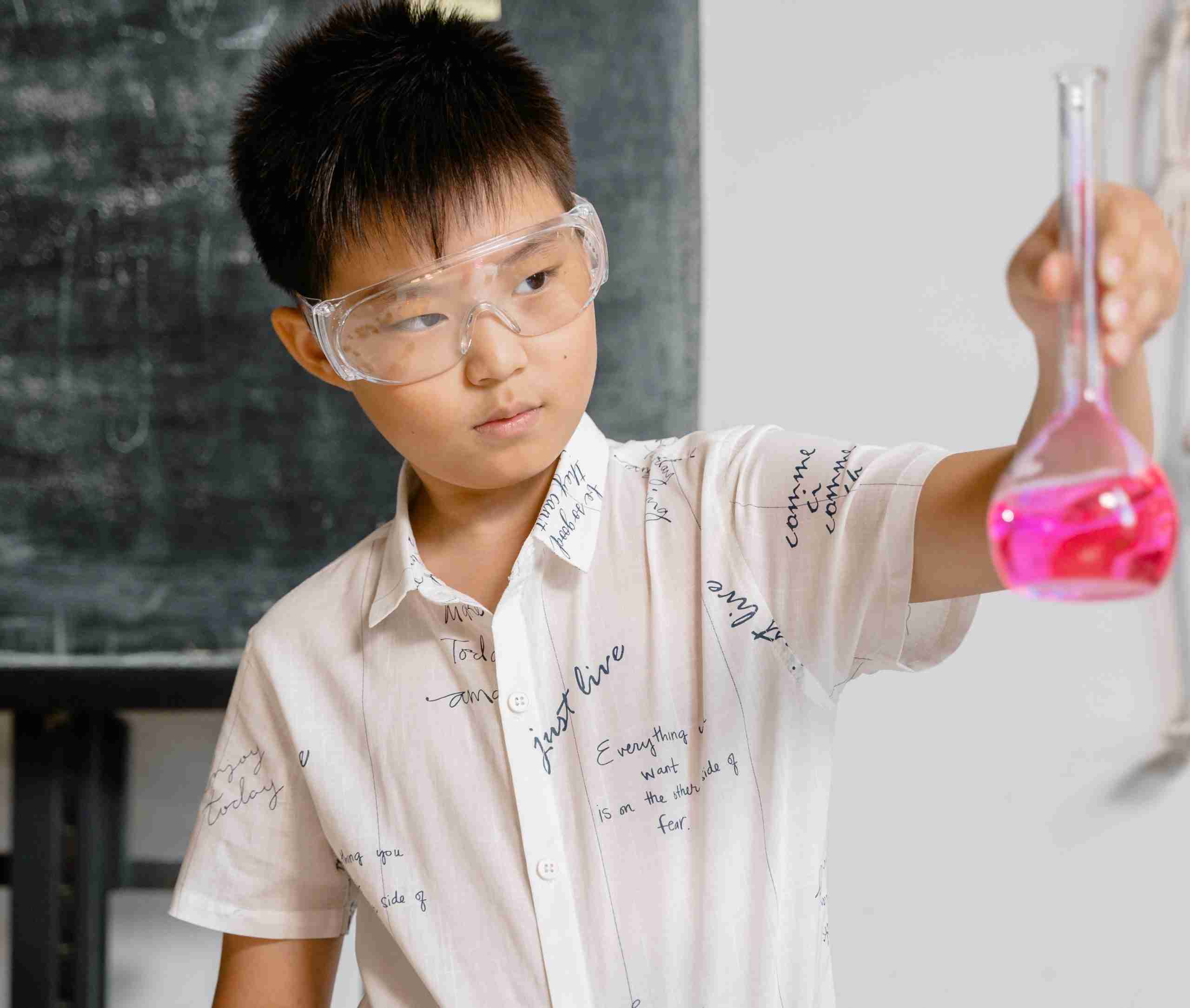 Boy in science class, with goggles, holding a beaker with bright pink content
