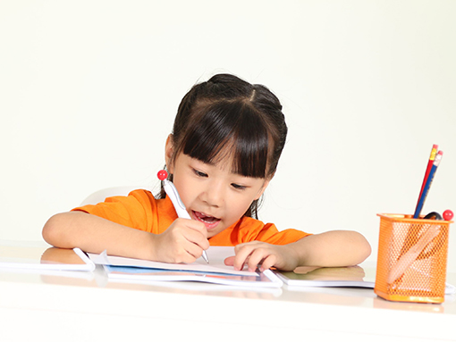 K2 girl in orange, happily working on her The Eton Academy worksheets
