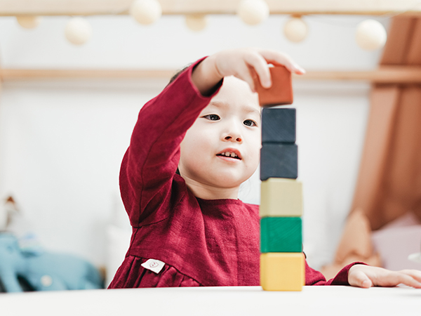 Little girl in red, stacking and balancing colourful wooden blocks