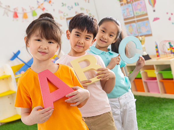 Three children, in a classroom environment, holding up the letters ABC