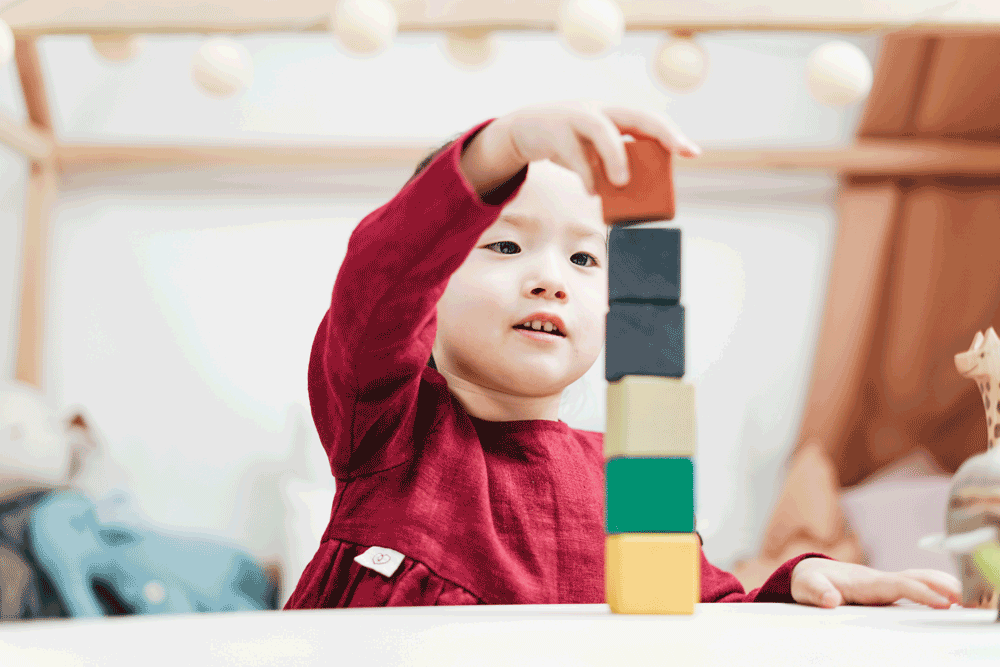Little girl in red, stacking and balancing colourful wooden blocks