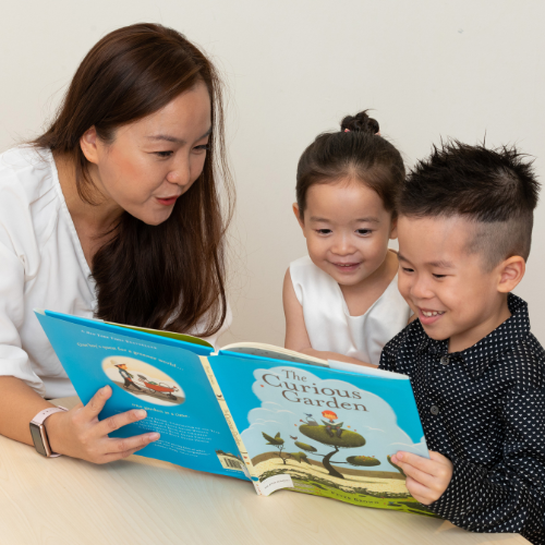Two children reading a book with a teacher